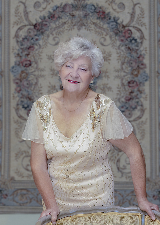 Senior woman in vintage gown standing by an antique chair. Fashion photography